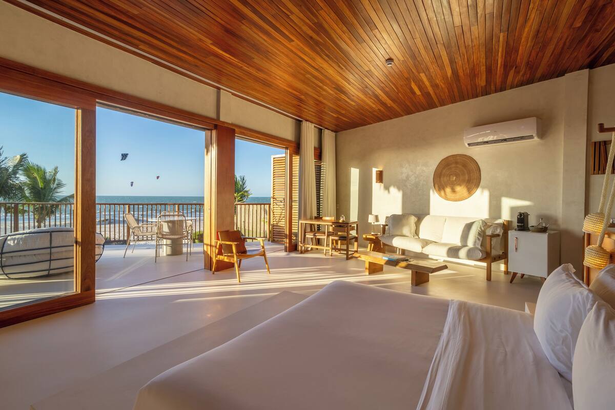 Una habitación amplia con una cama grande, techo de madera y vista a la playa.