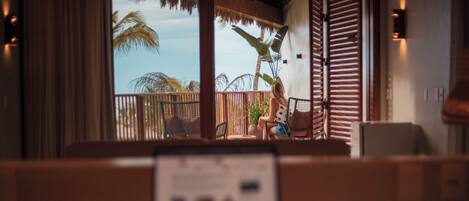 Une chambre avec vue sur les palmiers et un balcon. On aperçoit une chaise et une table au premier plan.