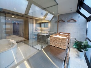 Une salle de bain moderne avec une douche à parois de verre, une baignoire sur pieds, un grand meuble-lavabo en osier et une plante en pot.