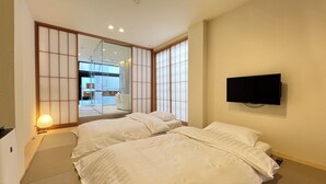 Une chambre d’hôtel avec deux lits, un téléviseur fixé au mur et un paravent coulissant de style japonais.
