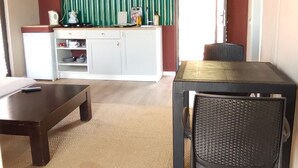 Uma sala de estar com teto escuro, um armário branco com eletrodomésticos de cozinha, uma mesa de jantar e uma cadeira, e um tapete bege.