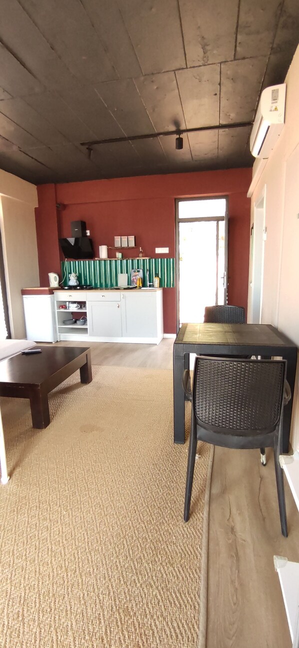 Ein Wohnzimmer mit dunkler Decke, einem weißen Schrank mit Küchengeräten, einem Esstisch und einem Stuhl sowie einem beigen Teppich.