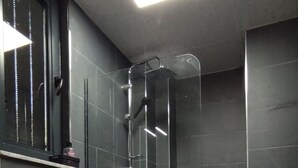Casa de banho moderna com sanita, chuveiro e cabine de duche com paredes de vidro.