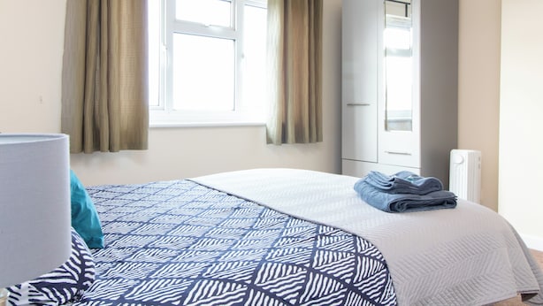 Un dormitorio con cama, armario, ventana con cortinas y radiador.