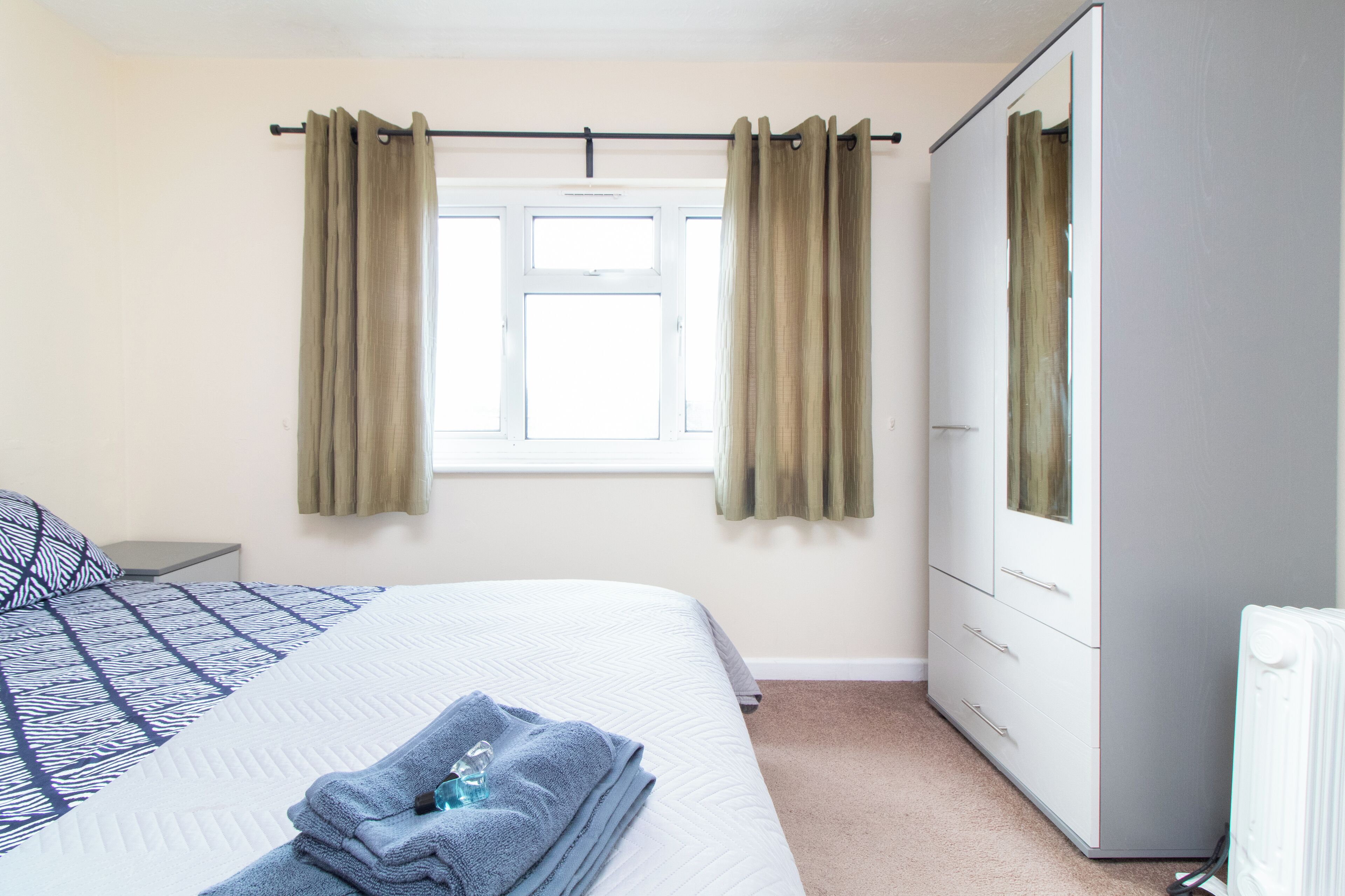 A bedroom with a bed, a wardrobe, a radiator, and a window with curtains.