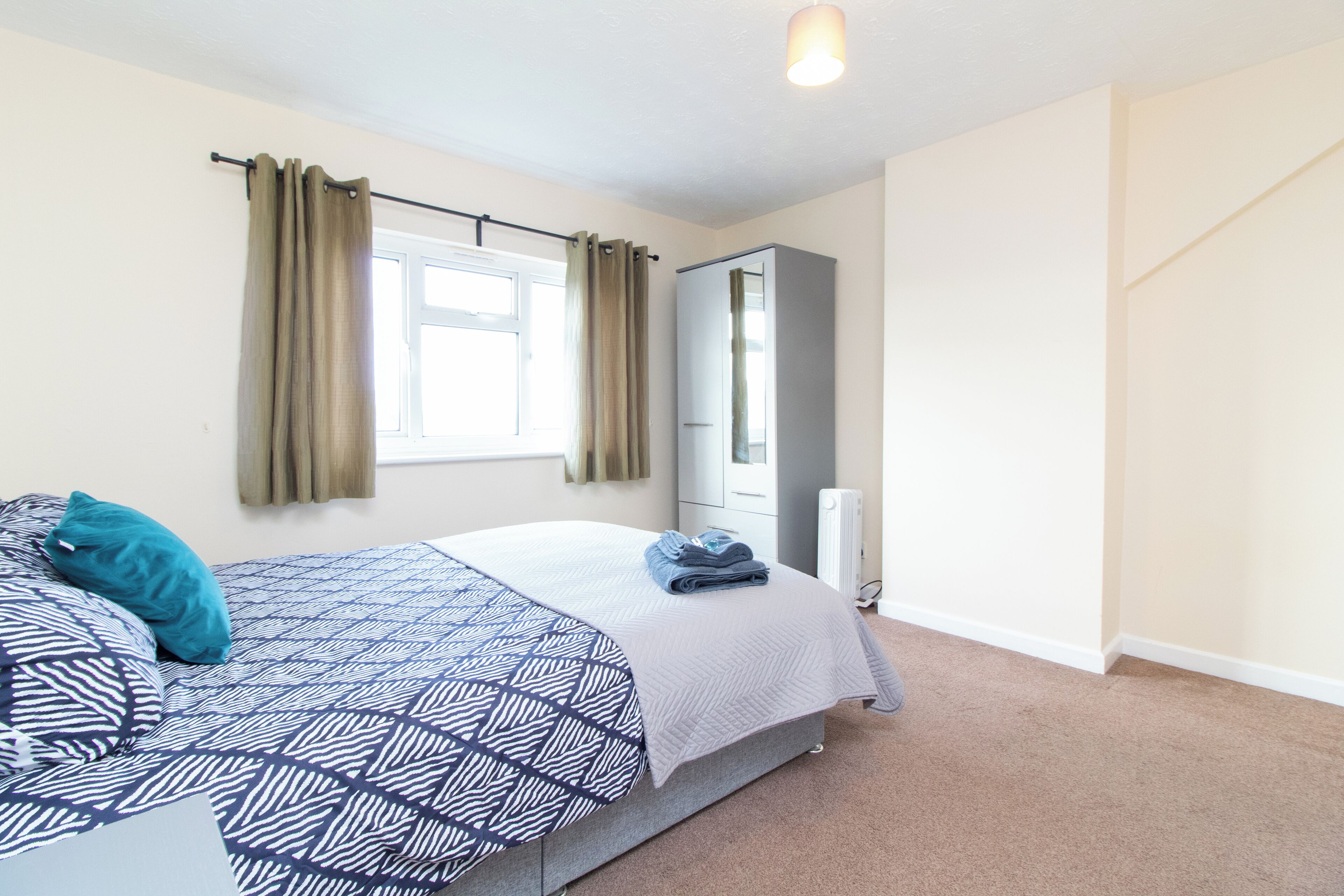 A bedroom with a bed, a wardrobe, a radiator, and a window with curtains.