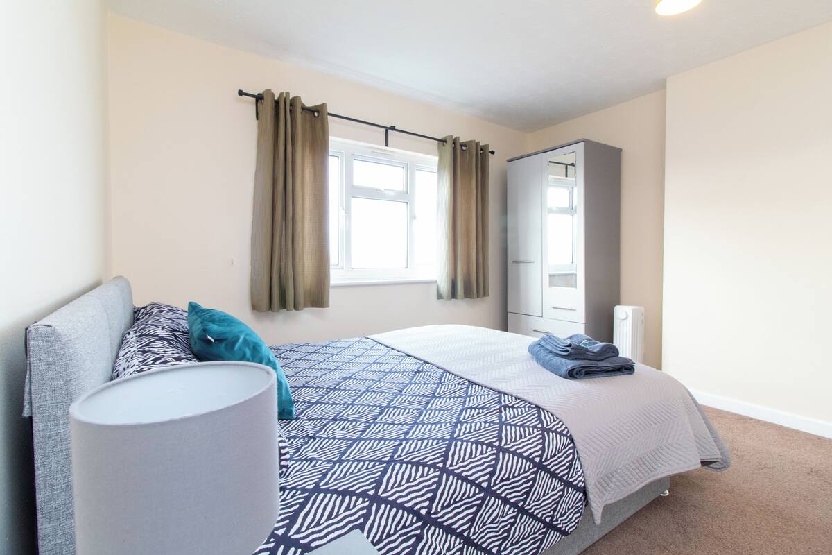 A bedroom with a bed, a wardrobe, a radiator, and a window with curtains.