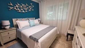 Um quarto com cama, mesas de cabeceira, penteadeira e uma obra de arte na parede.