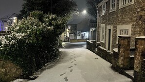 A snow-covered street with footprints leading towards a stone building with multiple windows.
