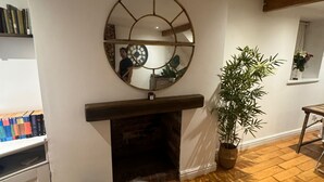 A living room with a fireplace, a round mirror, a sofa, a potted plant, and a bookshelf.