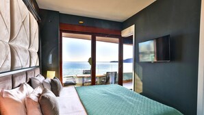 A hotel room with a large bed, a TV on the wall, and a view of the sea. - Royalis Suites Rafailovici - Beachfront Sea View Apartments (Becici)