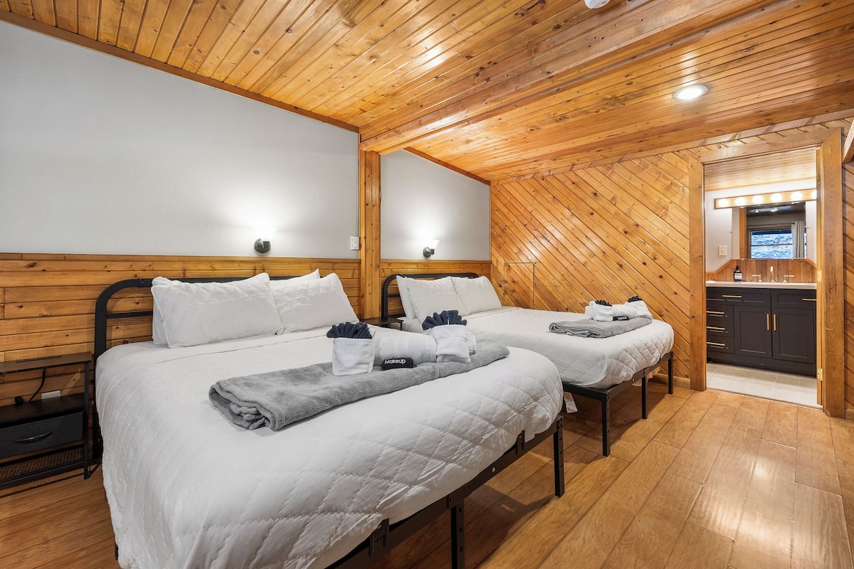 A room with two beds, wooden walls, and a small kitchenette.
