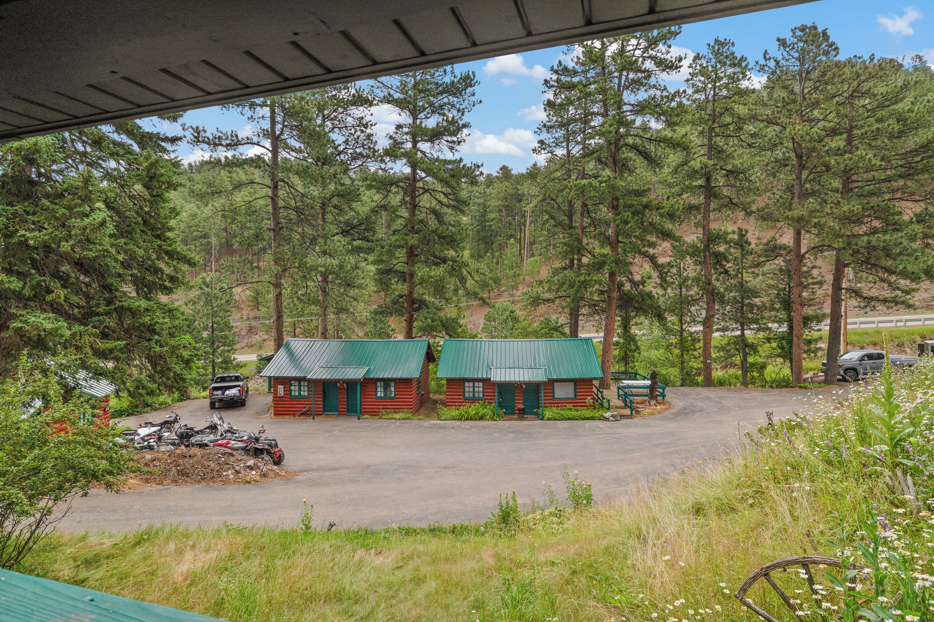 Een chalet met een groen dak, omgeven door een bos. Quadbikes staan ervoor geparkeerd.