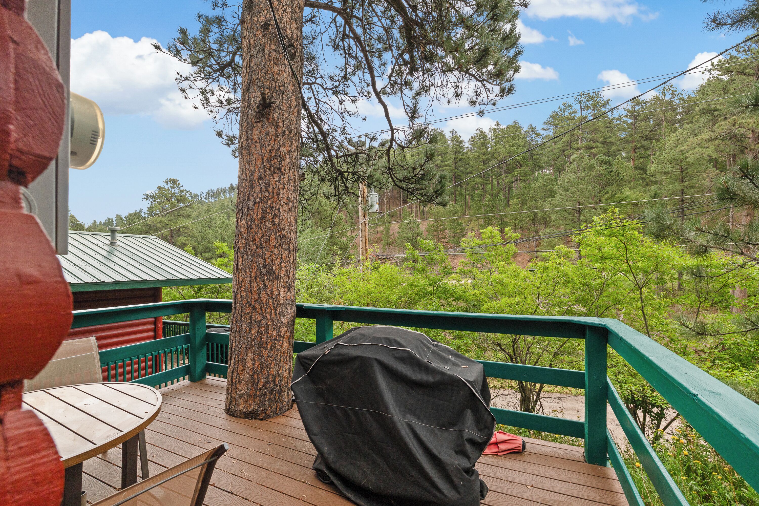 A wooden deck with a covered grill, a table, and a chair.