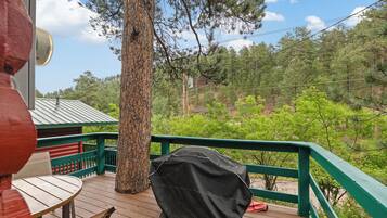 A wooden deck with a covered grill, a table, and a chair.