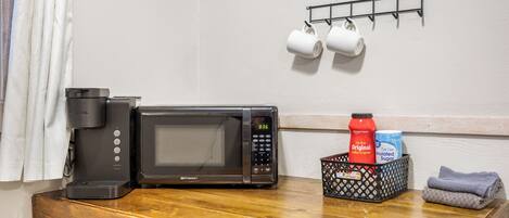 A kitchen counter with a coffee maker, microwave, and a basket containing a bottle and sugar packets.
