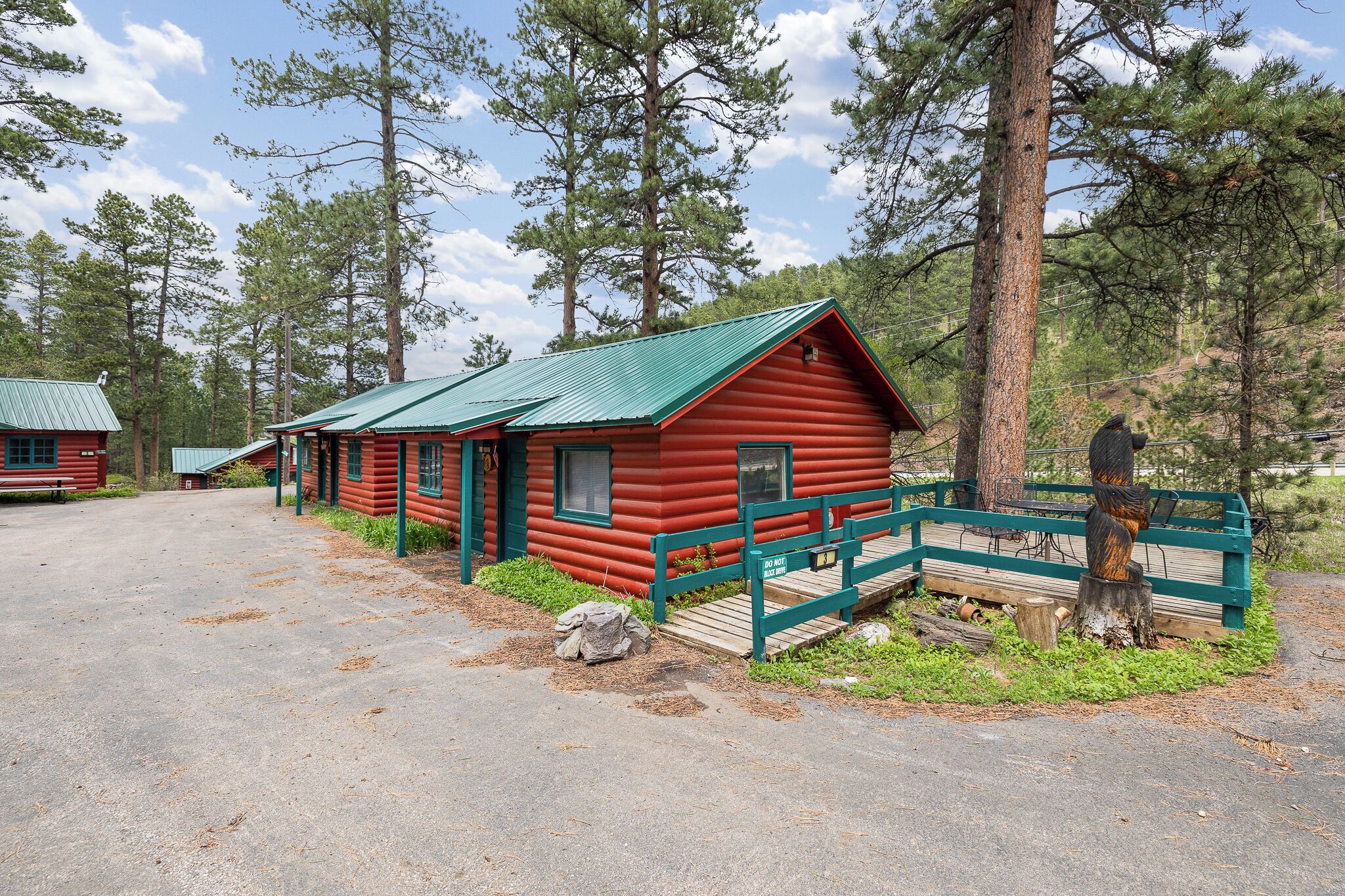 A red log cabin with a green roof, surrounded by tall pine trees.