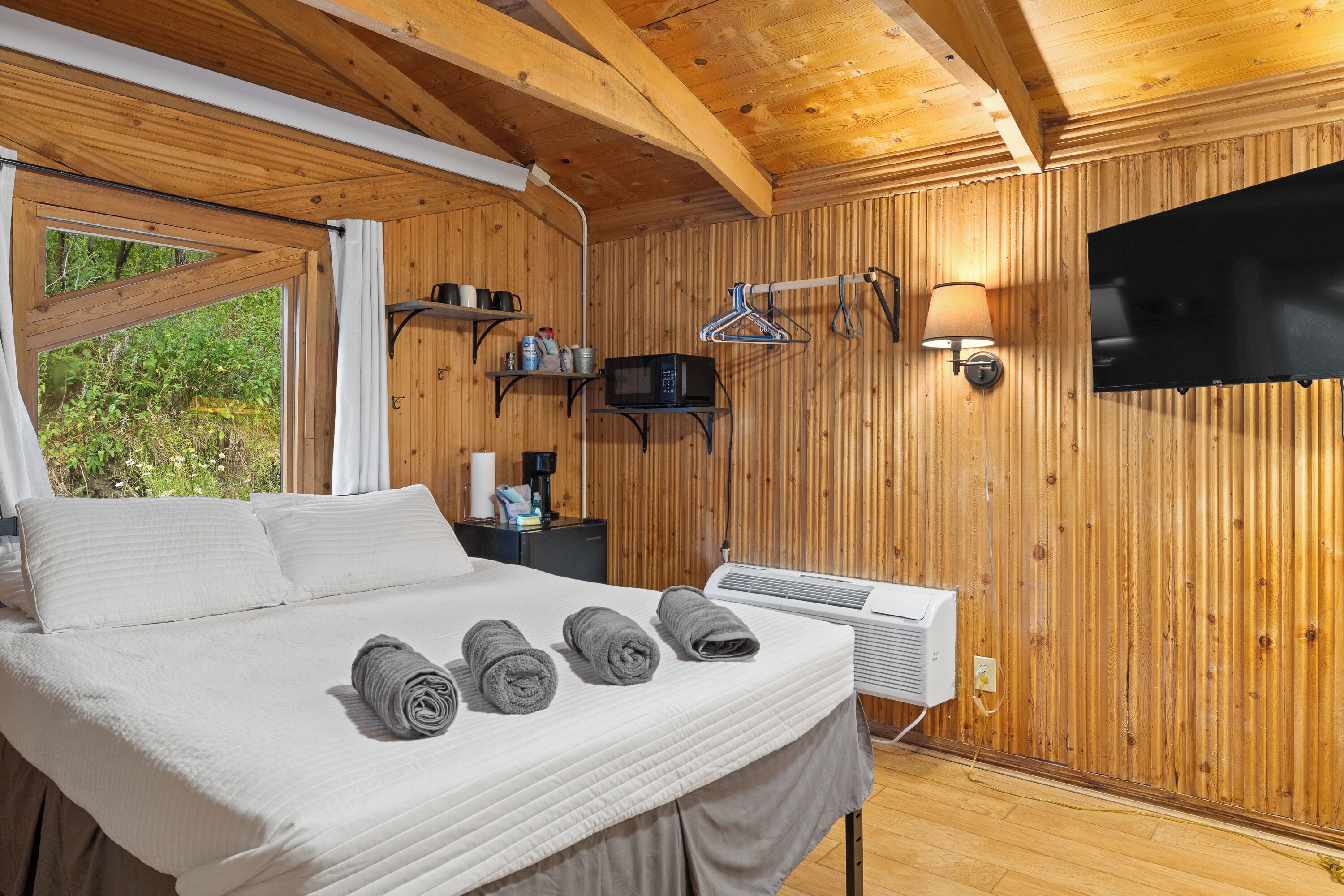 Una habitación tipo cabaña de madera con una cama, toallas, un televisor y un calentador.
