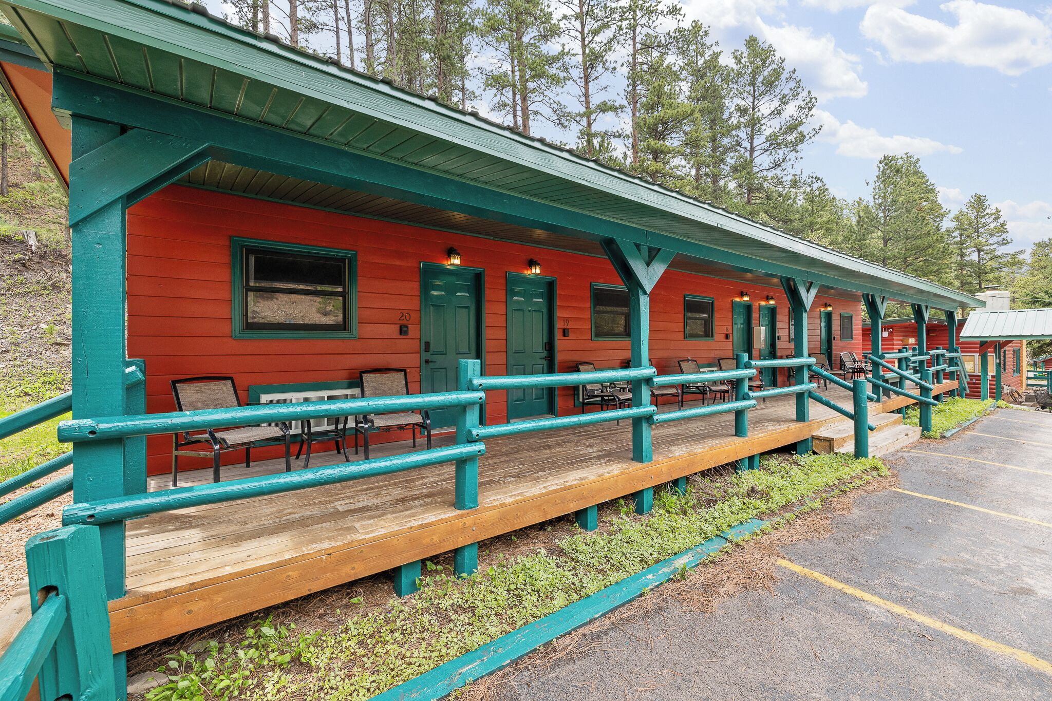 A red building with green trim and numbered doors, wooden benches, and a covered area with railings.