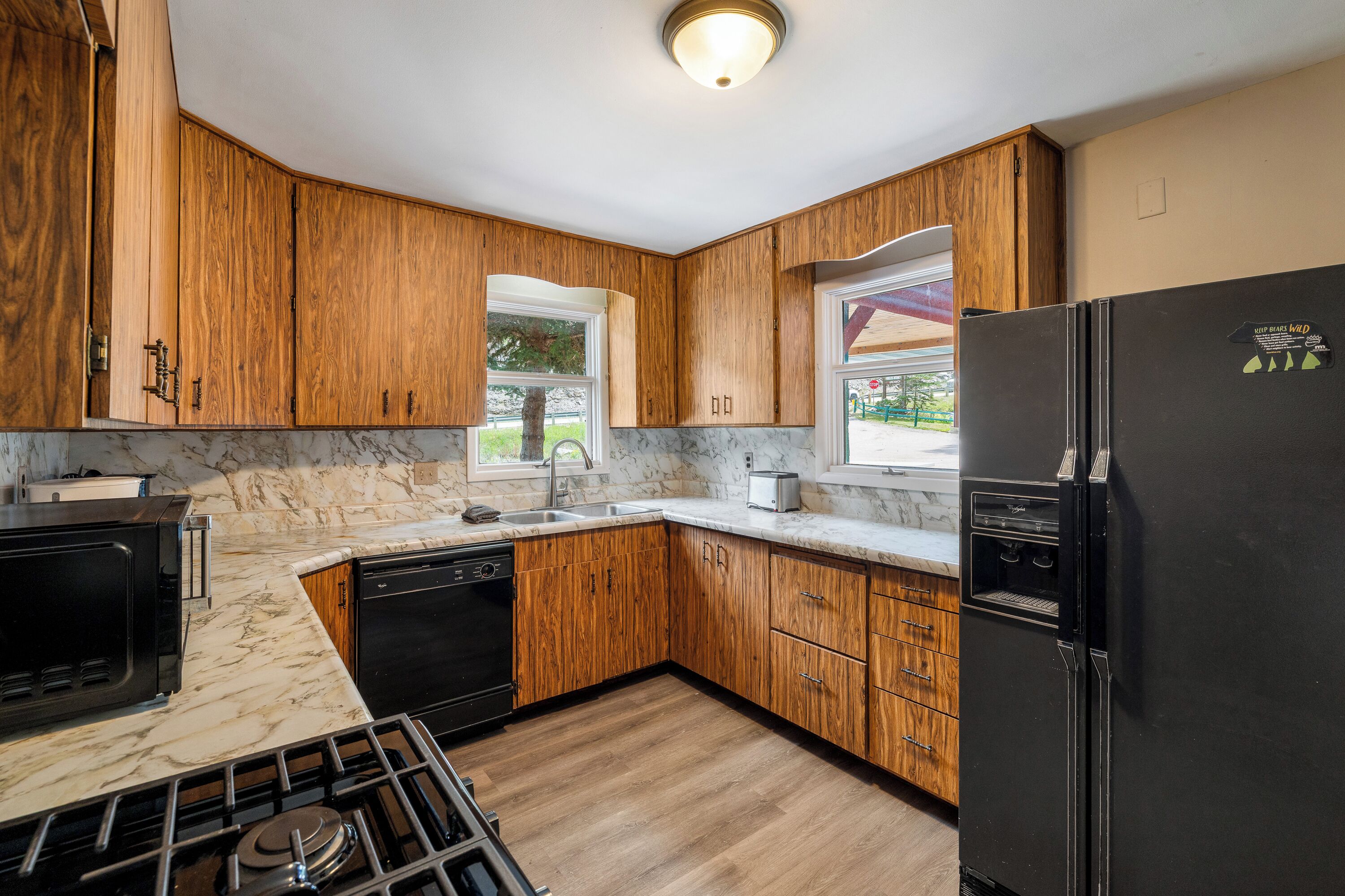 Una cocina con armarios de madera, un refrigerador negro, una estufa y una ventana con vistas al exterior.