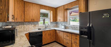 Una cocina con armarios de madera, un refrigerador negro, una estufa y una ventana con vistas al exterior.