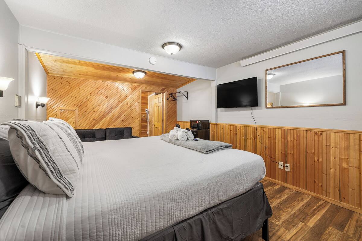 A bedroom with a large bed, wooden paneling, a flat-screen TV, and a mirror on the wall.