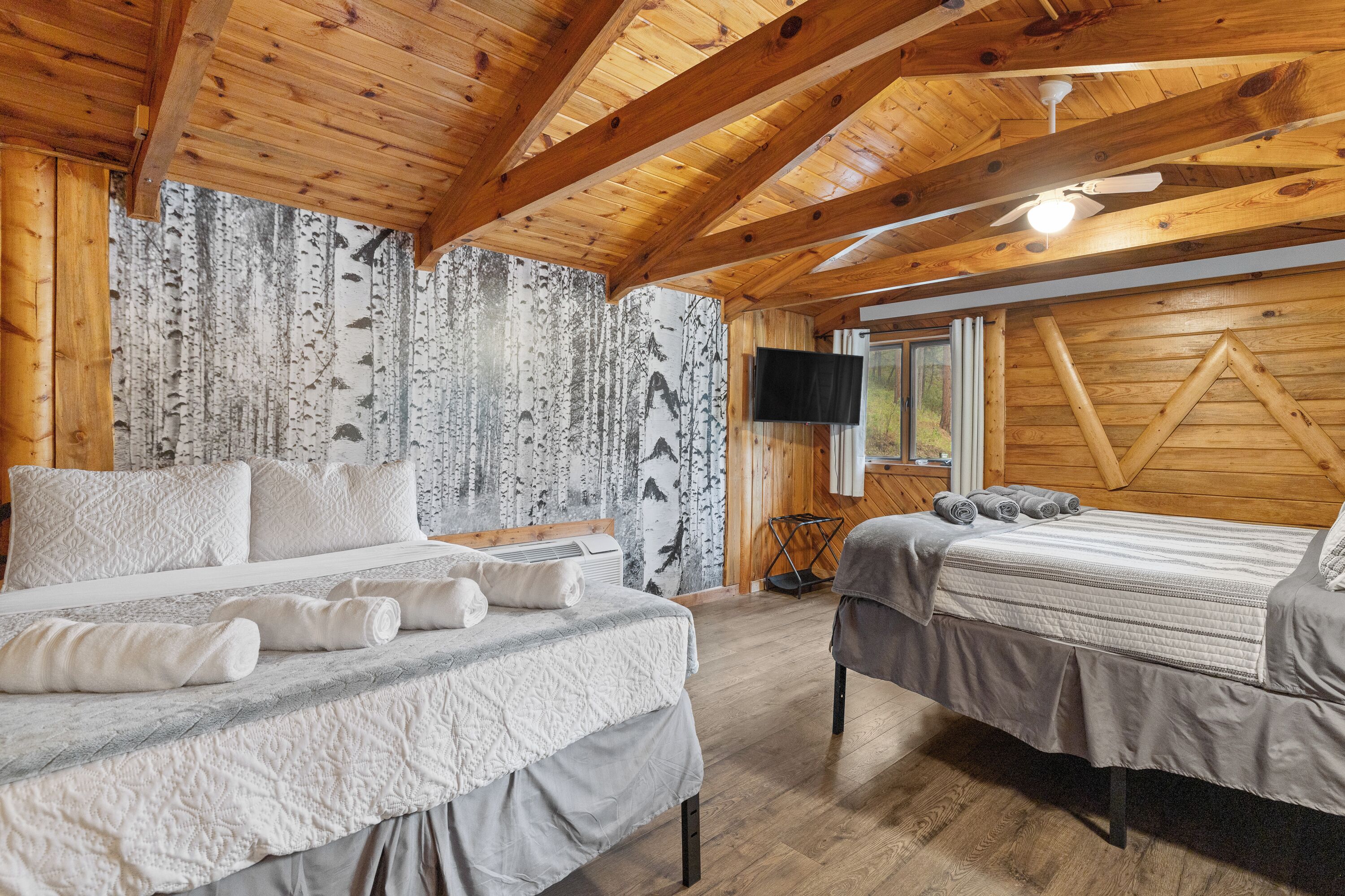 A wooden cabin bedroom with two beds, a ceiling fan, and a TV.