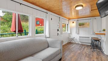 Un cuarto acogedor con sofá, piso de madera, ventanal con cortina roja y vistas a la vegetación.
