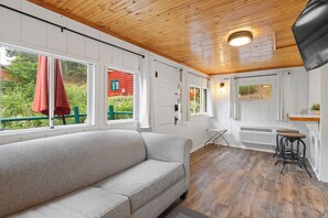 A cozy room with a sofa, wooden flooring, a window with a red curtain, and a view of greenery outside. - Ponderosa Pines (Lead)