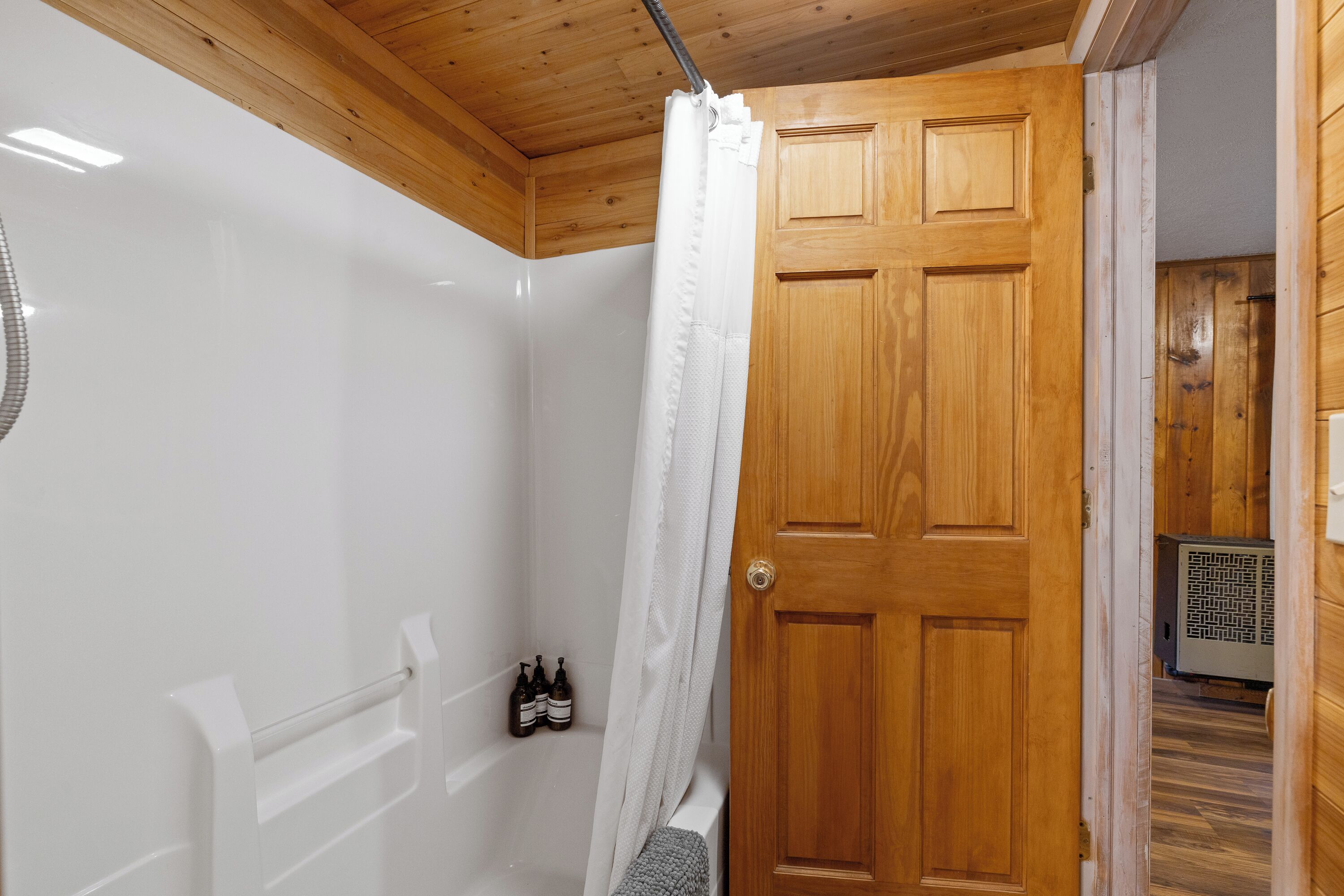 Una puerta de madera con una cortina de ducha blanca, una bañera blanca y una toalla en el suelo.