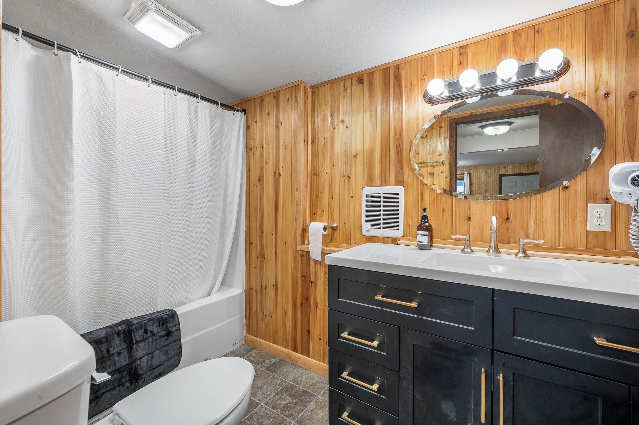 A bathroom with a wooden wall, a white toilet, a black vanity with a mirror, and a shower curtain.