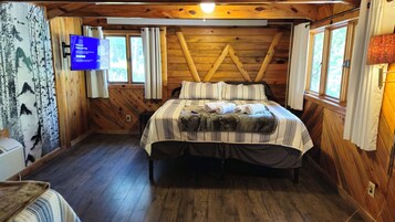 Habitación de cabaña de madera con cama, televisor y ventana.