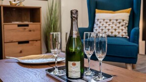 A bottle of champagne on a tray with four glasses, a wooden table, a blue sofa with patterned cushions, and a globe on a shelf. - Les Charmettes (Brides-les-Bains)
