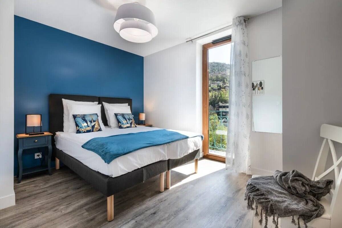 Un dormitorio moderno con una cama grande, una mesita de noche, una silla y vistas al verdor exterior.