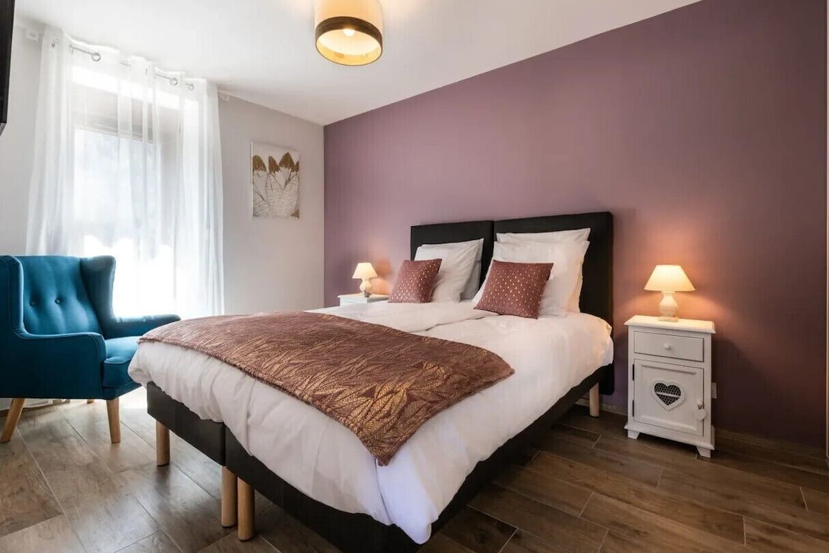 Un dormitorio con una cama, una silla, una mesita de noche y un cuadro en la pared.