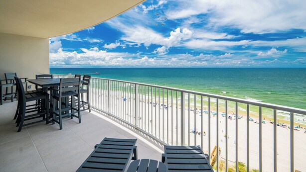 A balcony with a table and chairs, overlooking a beach with people and umbrellas. - New Beachfront Condo! Family Fun in Gulf Shores – PGS2 1402 (Gulf Shores)