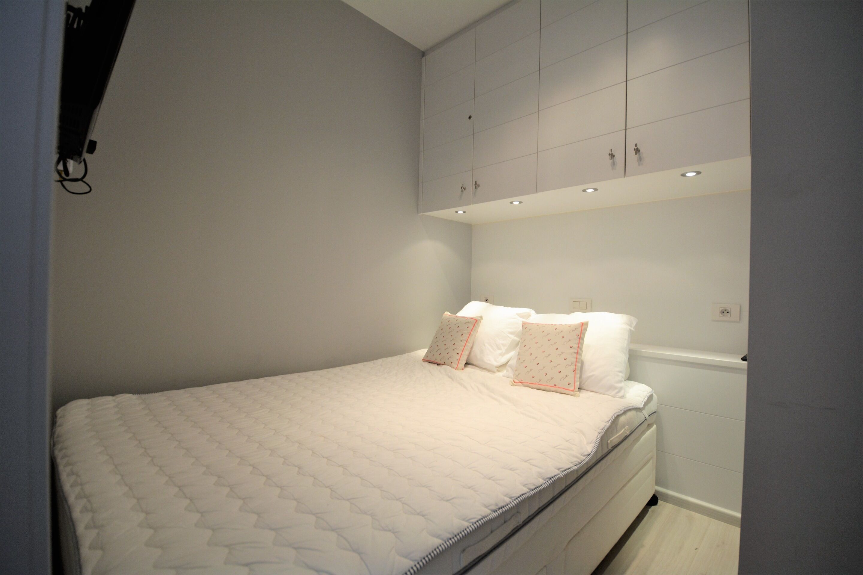 A bedroom with a bed, white walls, and a ceiling with cabinets.