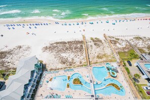 Vista aérea de un complejo turístico con piscina, sombrillas de playa y un paseo marítimo.