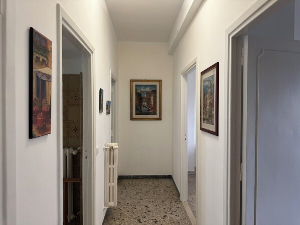Un pasillo con paredes blancas, un radiador y tres cuadros en las paredes.