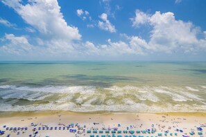 A beach with waves, a clear sky, and umbrellas.