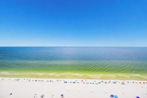 A beach with clear blue water, white sand, and umbrellas.