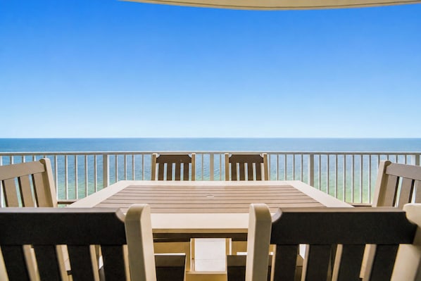A table with chairs on a balcony overlooking the sea.