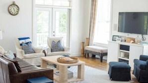 A living room with a sofa, armchair, coffee table, ottoman, TV, and a bookshelf. - Large Common Areas, Quiet Street, Golf Cart Available! (Carolina Beach)