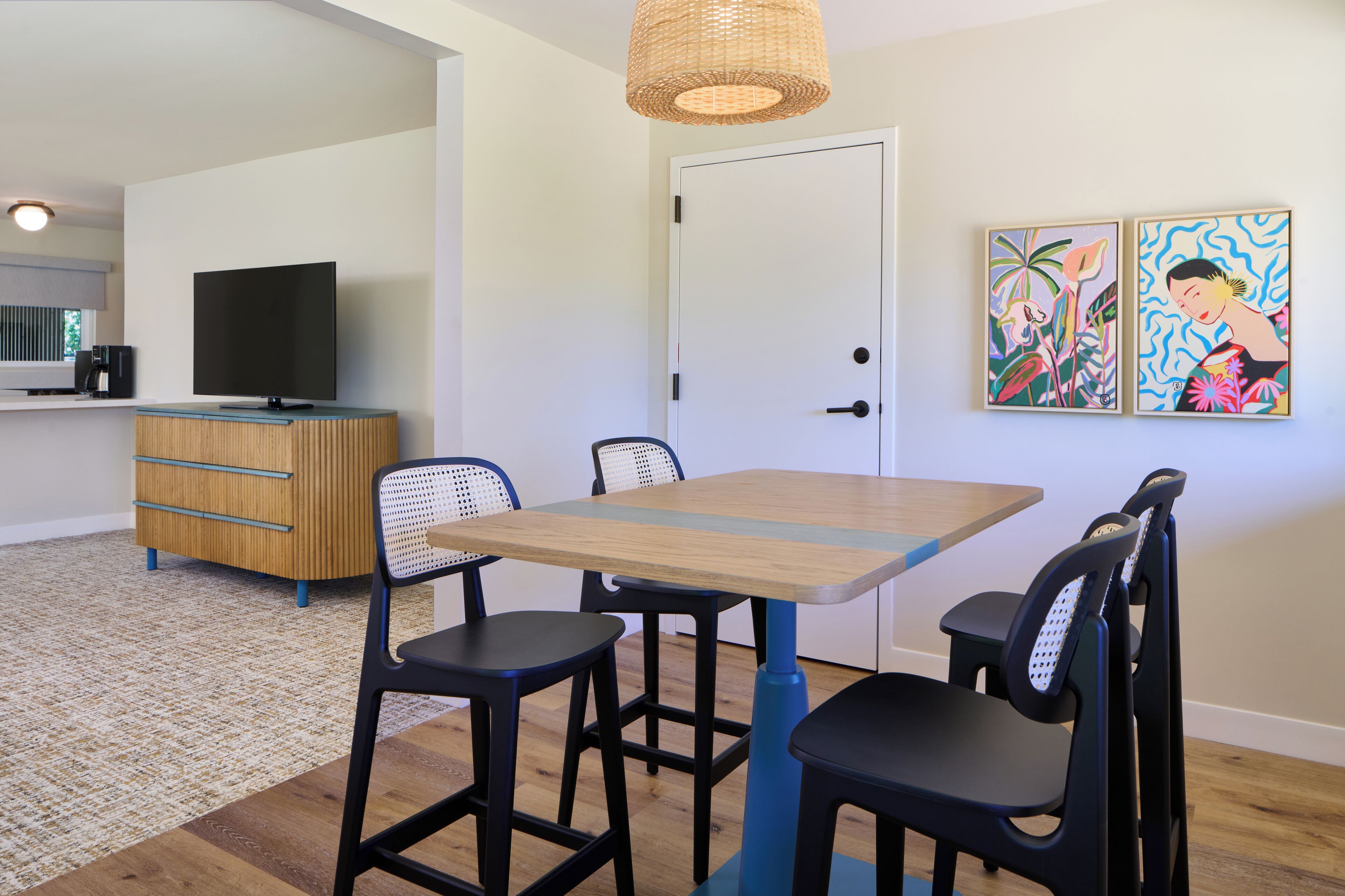 Un comedor moderno con una mesa de madera y sillas negras, un televisor y obras de arte en la pared.