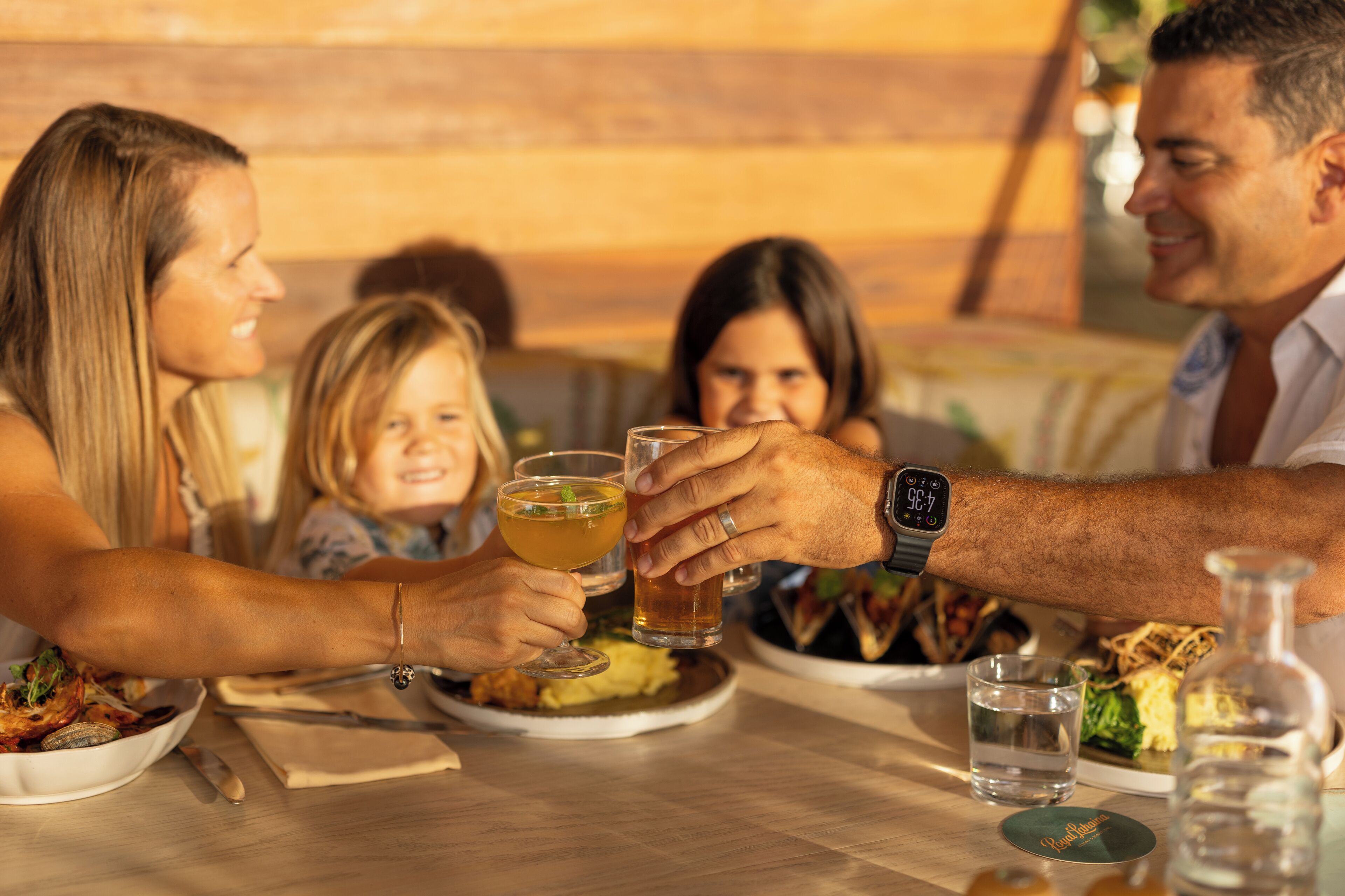 Una familia cenando en un restaurante de interior de madera, con una mesa llena de platos de comida, vasos y una botella de agua.