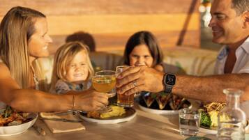 Una familia cenando en un restaurante de interior de madera, con una mesa llena de platos de comida, vasos y una botella de agua.