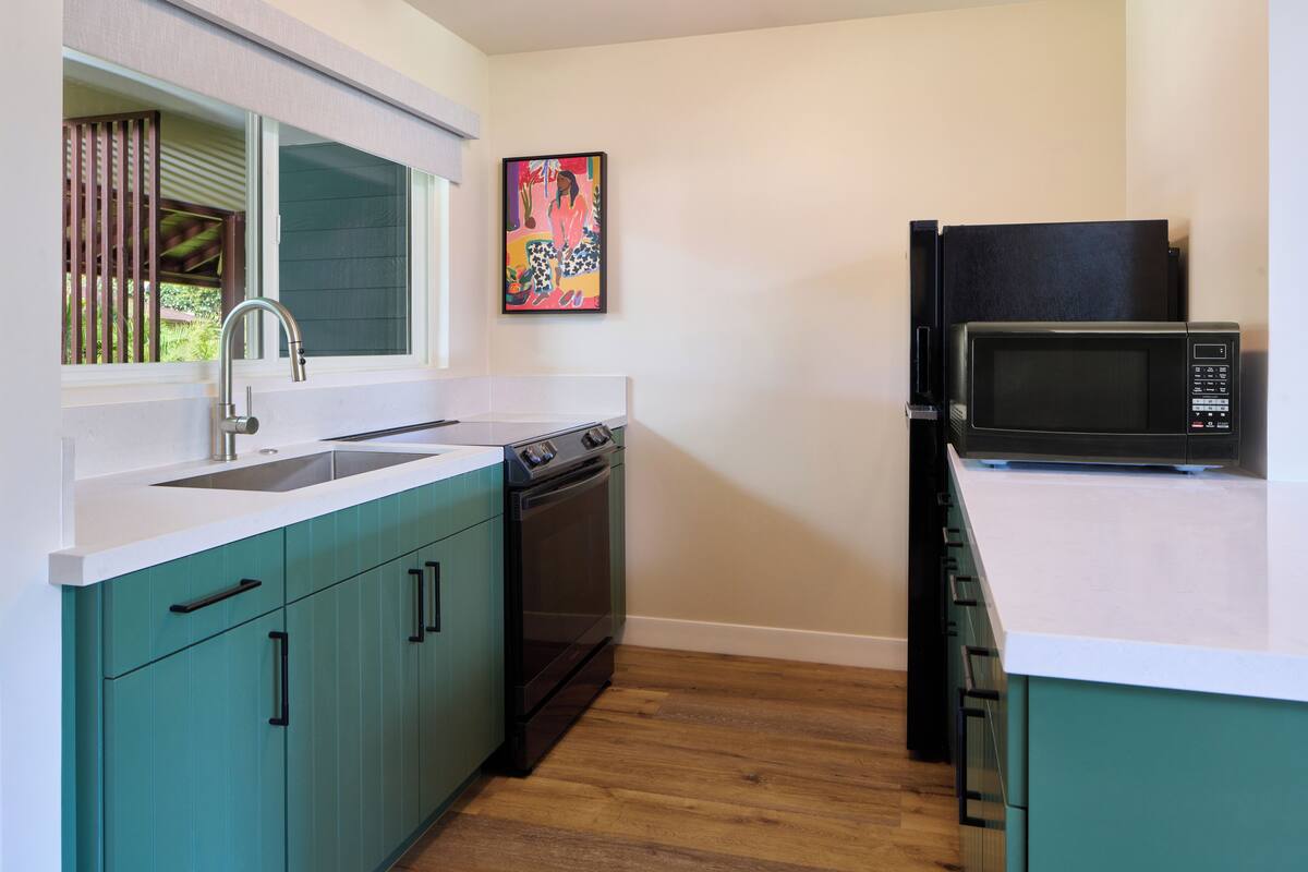Una cocina moderna con gabinetes color turquesa, encimera blanca, pileta de acero inoxidable, lavavajillas y microondas negro.