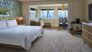 Una habitación de hotel con una cama grande, un escritorio con silla, vista al océano y un balcón con lámpara colgante.