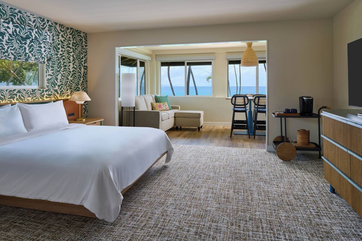 Una habitación de hotel con una cama grande, un escritorio con silla, vista al océano y un balcón con lámpara colgante.