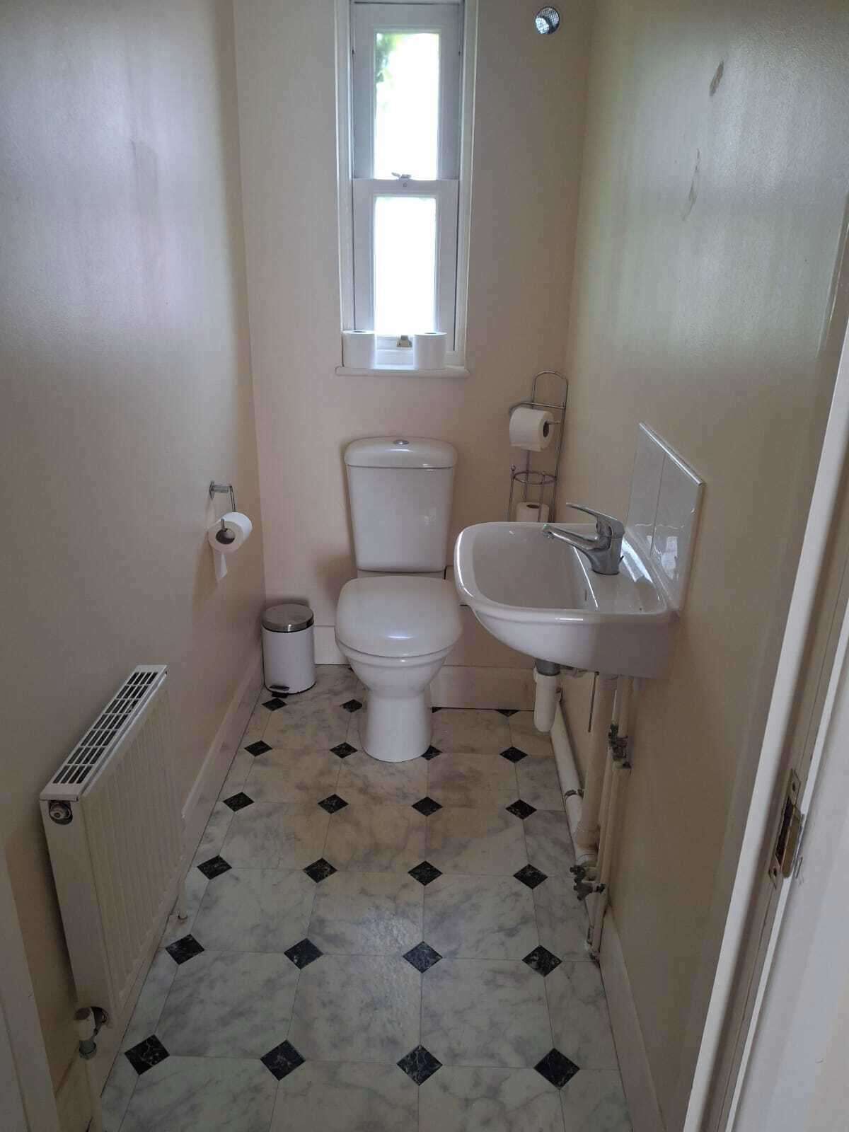A small, narrow bathroom with a toilet, sink, and a window above the toilet.